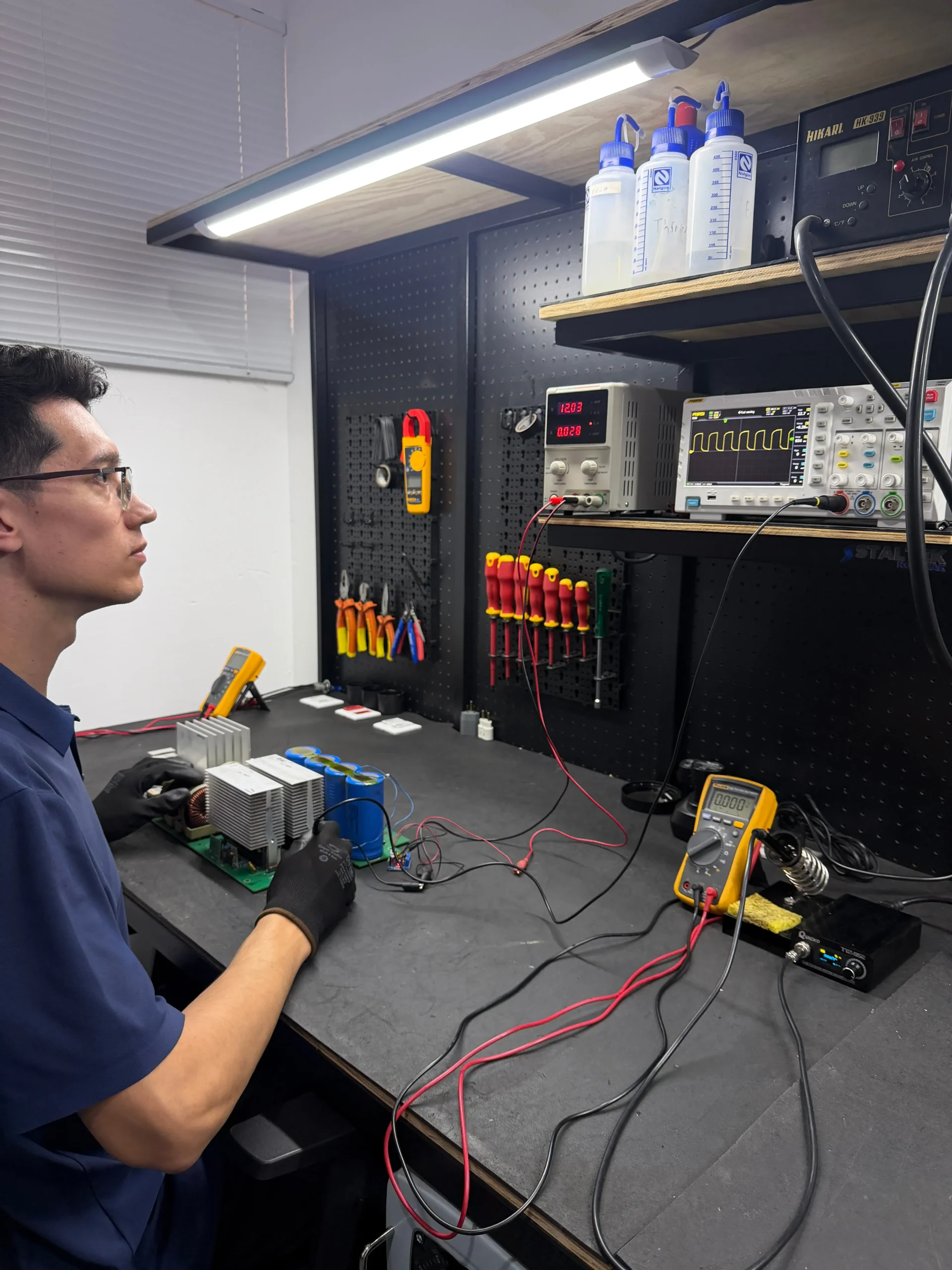 Técnico especializado da Staltek analisando placa eletrônica de nobreak com osciloscópio e multímetro, utilizando óculos de proteção e luvas para diagnóstico de falha de nobreak.