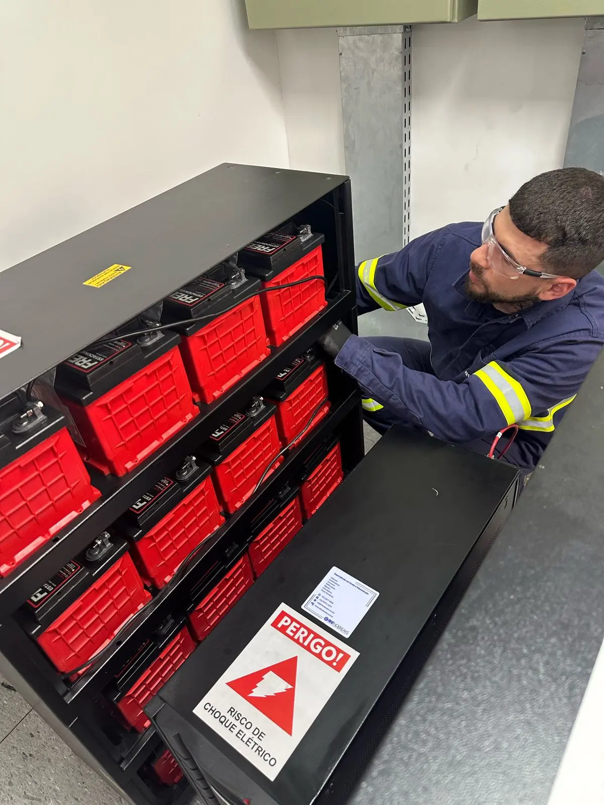 Técnico especializado realizando manutenção preventiva em banco de baterias Freedom estacionárias de um nobreak corporativo profissional, utilizando equipamentos de proteção individual.